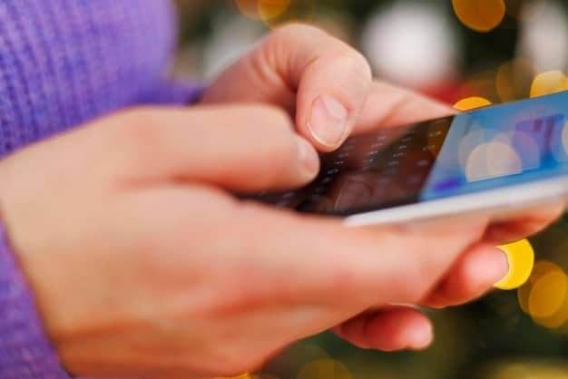 A person using a smartphone to check their credit card rewards balance, with a notification icon highlighted on the screen. The background shows a blurred image of an online banking website. The overall image conveys the idea of actively managing and tracking rewards.