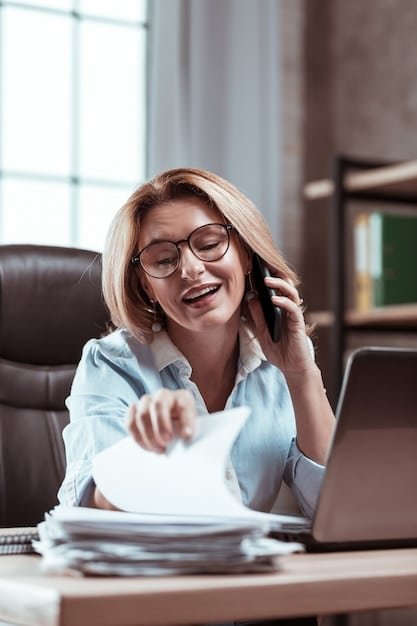 A smiling person talking on the phone with a financial advisor with laptop and notebook on a table..